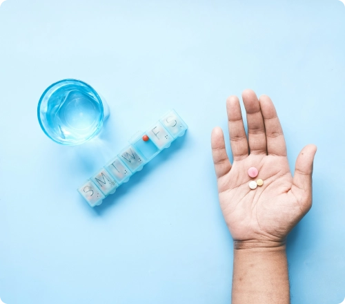 Image of a pill box, glass of water and outstretched hand holding pills to demonstrate Pharmacy products that can be sent with Sherpa